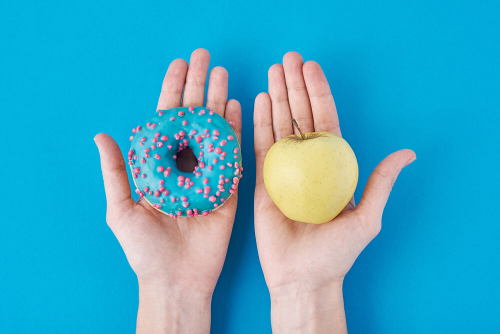 Modrý donut a žluté jablko v rukou na modrém pozadí